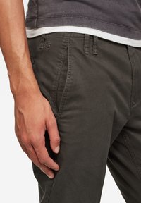 Ciemnozielone spodnie z mieszanki bawełny o wąskim kroju, wyposażone w boczne kieszenie i przeszycia. Mały akcent z logo blisko pasa.