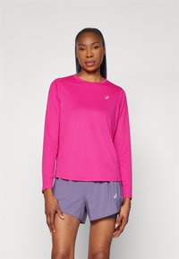 Fuchsian långärmad sporttröja med rund halsringning, kombinerad med ljuslila nätshorts. Har en subtil logotyp på bröstet.