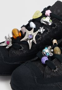 Baskets noires décorées de breloques colorées en forme d’étoile et de perles enfilées sur les lacets.