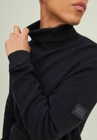 Navyblauwe geribde coltrui met lange mouwen en een gestructureerde brei. Kenmerkt zich door een merkembleem op de linkerarm.