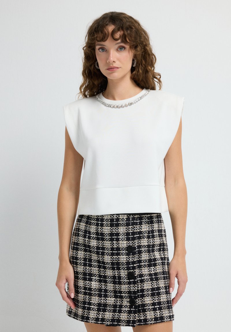 Top blanco estructurado con mangas cortas y un escote de joyas, combinado con una falda a cuadros en blanco y negro con botones.