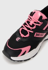 Sneaker sportivo nero e rosa con tessuto texturizzato, lacci rosa e accenti neri. Presenta una suola bianca e un dettaglio del logo sul lato.