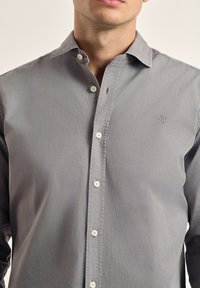 Camisa de botonada gris hecha de algodón con una textura suave. Cuenta con un collar, cierre de botones en el frente y un logo sutil en el pecho.