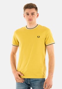 Camiseta de algodón amarilla con mangas cortas, cuello de canalé con franjas verdes y blancas, y un pequeño logo oscuro en el pecho.