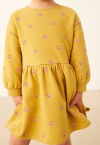 Vestido de felpa amarillo con patrones de arcoíris, mangas largas abullonadas, escote redondo y cintura fruncida. Textura suave y estilo casual.