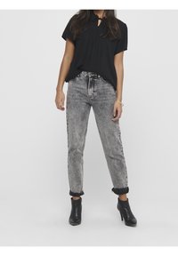 Haut noir à manches courtes avec un col en forme de goutte, associé à un jean en denim gris clair avec une coupe fuselée et des revers roulés. Bottines noires.