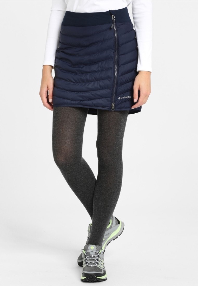 Marinblå isolerad kjol med quiltat mönster, som har en sidogylf och logotypdetalj. Matchad med mörka strumpbyxor och grå sportskor.