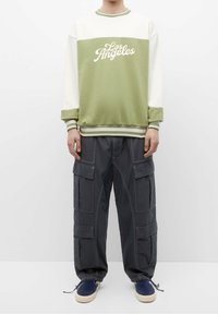 Groen-witte sweatshirt met "Los Angeles" opdruk, gecombineerd met grijze cargobroek met meerdere grote zakken en een ontspannen pasvorm.