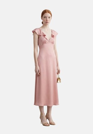 Giovane donna con un vestito midi rosa con maniche arricciate e bottoni, che tiene una piccola borsa oro e indossa sandali dorati con tacchi alti.