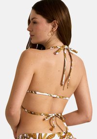 Bikinibroekje met halterbanden, voorzien van een bloemenpatroon in geel en wit, gemaakt van rekbare stof, met een design en details aan de achterkant.