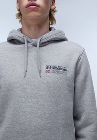 Hoodie grigia con coulisse, caratterizzata da un'etichetta con logo stampato sul petto. Il tessuto appare morbido e strutturato con un design casual.