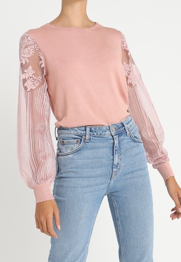 Blouse rose à manches longues avec dentelle et tissu transparent plissé sur les manches, associée à un jean taille haute bleu clair.