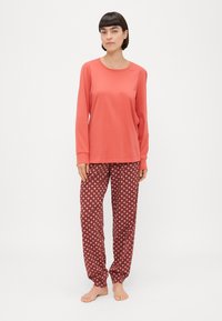 Lange mouw koraalkleurige top gecombineerd met gemusterde kastanjebruine broek met roze geometrische vormen. Zachte stof, ontspannen pasvorm, comfortabel ontwerp.