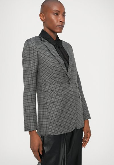 Blazer de cuadros grises con un corte entallado, cierre de botón sencillo, solapas de muesca y dos bolsillos delanteros. Combinado con una camisa negra texturizada.