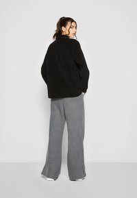 Zwarte corduroy overshirt met een kraag, gecombineerd met grijze wijde pantalon. De outfit heeft een relaxte pasvorm en een minimalistisch ontwerp.
