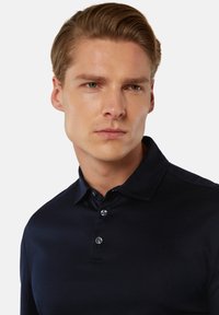 Navy blauwe polo shirt gemaakt van soepele stof, met een drieknoopsluiting en een klassieke kraag. Subtiele glans en een getailleerde pasvorm.