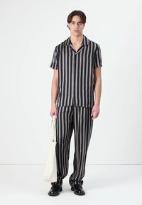 Camicetta a righe bianco e nero con maniche corte e pantaloni abbinati, tessuto leggero, vestibilità rilassata, indossata con una borsa a tracolla crema.
