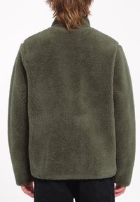 Chaqueta de forro polar en verde oliva, con una superficie texturizada, cuello alto y un corte relajado. El tejido es suave y cálido, con un aspecto acogedor.