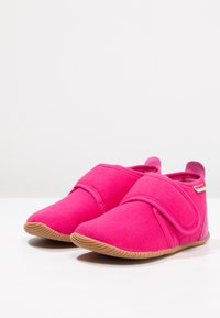 Różowe materiałowe klapki z rzepem, zaokrąglonym noskiem i elastyczną gumową podeszwą. Gładka tekstura z subtelnymi detalami w szyciu.