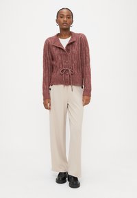 Μπορντό ζακέτα με πλέξη καλώδιο, γιακά, μπροστινά κουμπιά και ζώνη στη μέση. Συνδυασμένη με εκρού παντελόνι φαρδιάς γραμμής και μαύρα παπούτσια με πλατφόρμα.