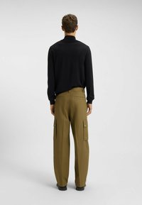 Black long-sleeve shirt with a high collar, paired with loose, olive green cargo pants featuring side pockets and a smooth fabric texture.