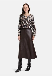 Long brown leather skirt paired with a black and beige floral-patterned blouse. Model wears knee-high black heeled boots.