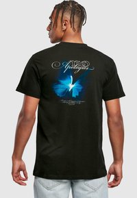 Sort t-shirt med et stort blåt sommerfugle-grafik på ryggen, med stiliseret hvid tekst ovenfor og under designet.
