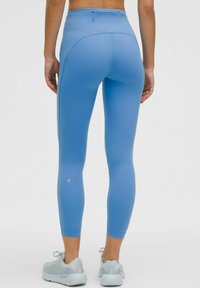 Lichtblauwe high-waisted leggings van een glad, stretchy materiaal. Heeft een naadloos ontwerp en een subtiele logo nabij de enkel.