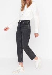 Jean taille haute noirs avec une jambe fuselée, design à cinq poches et un léger effet usé, associés à une chemise blanche à rayures avec boutons.