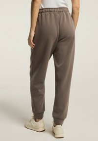 Brązowe dresy z miękkiego materiału, z elastycznym pasem i ściągaczami na nogawkach, o tapered leg designie i gładkiej fakturze.