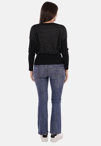 Maglione nero in maglia con un retro texture, abbinato a jeans svasati blu e sneakers bianche. Il maglione presenta un orlo a costine e maniche lunghe.