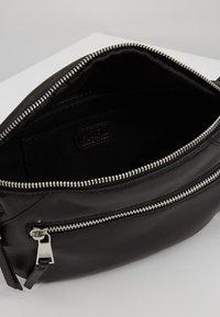 Borsa in pelle nera con esterno liscio, dettagli in cerniera argentata e interno foderato. Presenta un compartimento principale e una tasca zip più piccola.