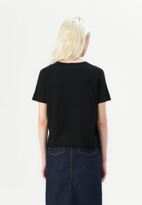 T-shirt noir à manches courtes avec un col rond, texture douce et ourlet droit, associé à une jupe en denim foncé avec des poches arrière.