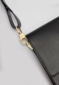 Czarna skórzana torba na ramię o gładkiej fakturze, z metalowym zapięciem w kolorze złota oraz regulowanym paskiem, oferująca różnorodne opcje noszenia.