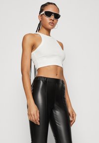 Bílý proužkovaný crop top a černé kalhoty s vysokým pasem z umělé kůže. Model má bílé sluneční brýle a dlouhé zapletené vlasy.