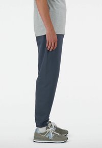 Camiseta gris de manga corta combinada con pantalones jogger azul marino. Los joggers tienen puños elásticos. Lleva zapatillas gris y azul con una suela clara.