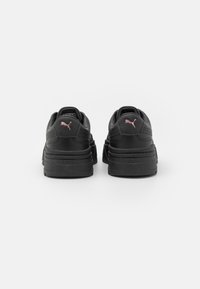 Schwarze Sneaker mit einem Obermaterial aus strukturiertem Leder, dickerer Sohle und einem pinken Puma-Logo an der Ferse. Minimalistisches Design mit abgerundeter Form.