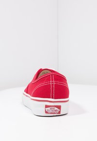 Rød kanvas slip-on sko med hvit gummisole og røde detaljer. Har en fremtredende "VANS OFF THE WALL" logo på hælen.