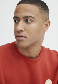 Rode sweatshirt met korte mouwen, voorzien van een ronde halslijn en een textuurstof, met een crèmekleurig rond logo-detail op de voorkant.