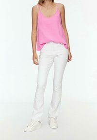 Růžový lehký top bez rukávů se špagetovými ramínky, spárovaný s bílými úzkými džíny a bílými teniskami. Texturovaná látka, volný střih.