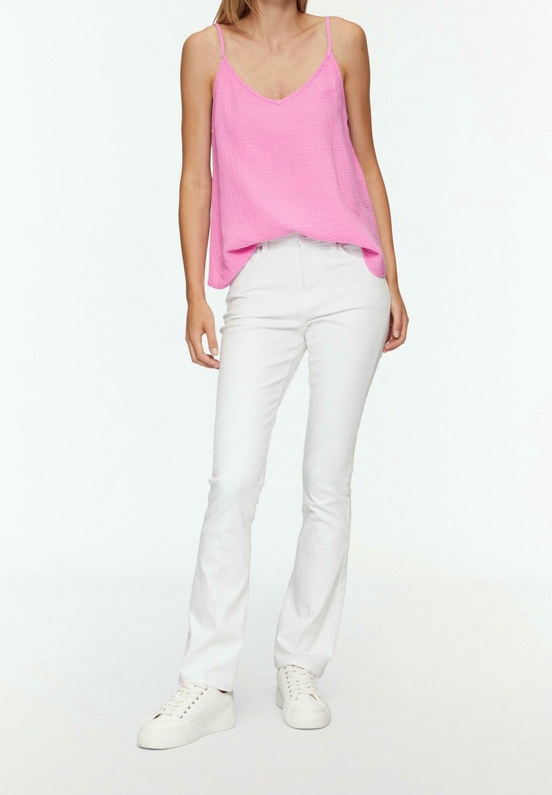 Růžový lehký top bez rukávů se špagetovými ramínky, spárovaný s bílými úzkými džíny a bílými teniskami. Texturovaná látka, volný střih.