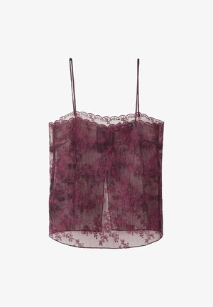 Kobieta o długich blond włosach, ubrana w przezroczysty, ciemnofioletowy koronkowy top, czarne ramiączka, złoty naszyjnik typu choker z zawieszką i brązowy futrzany płaszcz.