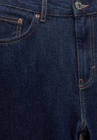 Dark blue denim jeans with copper rivets, contrasting yellow stitching, and a classic five-pocket design. Features a button closure and belt loops.