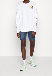 Camiseta blanca de manga larga con gráficos coloridos en las mangas, combinada con pantalones cortos de mezclilla y zapatillas verde menta.