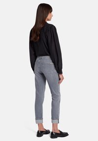 Blusa nera a maniche lunghe con dettaglio di ruches, abbinata a jeans in denim grigi con taglio dritto e orli risvoltati. Mocassini neri completano il look.
