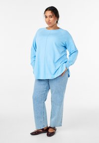 Hele sinine pikkade varrukatega topp ümmarguse kaelusega, koos hele triibulise teksapükstega ja tumepruunide madalate jalanõudega.