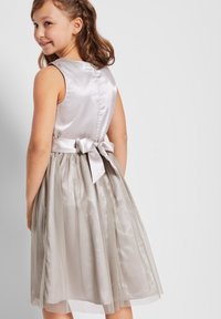 Robe en satin argenté avec un corsage ajusté, une jupe plissée et transparente, et un nœud en satin contrastant à l'arrière. Texture lisse et design élégant.