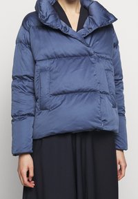 Granatowa kurtka puchowa z wysokim kołnierzem, ukośną kieszenią z przodu i pikowanym wykończeniem. Wykonana z gładkiego, lekkiego materiału.