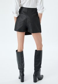 Pantaloni corti neri textured con vita alta, abbinati a stivali neri in pelle fino al ginocchio con tacco quadrato chunky.