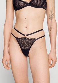 Conjunto de lingerie de renda preta com um soutien com aros e detalhes intrincados em renda, combinado com um fio dental com alças e um padrão floral.